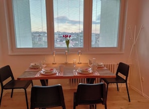 Ein Essbereich mit einem Tisch für vier Personen, vier Stühlen und Blick auf die Stadt durch große Fenster.
