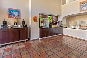 Un vestíbulo de hotel con mostrador de recepción, una máquina de café, un refrigerador y un mostrador con pasteles.