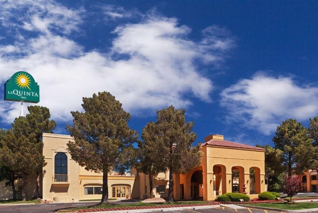 Un hôtel La Quinta Inn, avec un ciel bleu dégagé, une grande enseigne et un bâtiment doté de fenêtres en arc de cercle et d’un toit recouvert de tuiles.