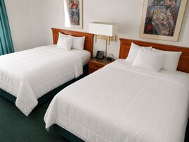 Dos camas contiguas con ropa blanca, una mesita de noche con lámpara y un cuadro en la pared.