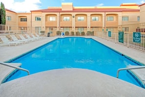 Una piscina con sillones de descanso y un edificio con techo de tejas rojas al fondo.