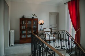 Ein Zimmer mit einem Holzregal, einer Stehlampe, einem weißen Heizkörper und einem roten Vorhang.
