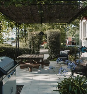 Ein überdachter Patio-Bereich mit Grill, Picknicktisch und Sitzgelegenheiten.