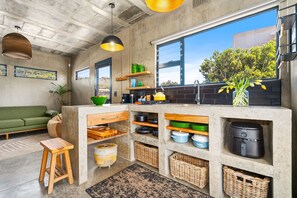 Una cocina moderna con una isla de hormigón, estanterías de madera y vistas al exterior.