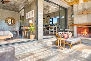 A modern living room with a fireplace, a dining area, and a kitchen visible through glass doors. - KOH Pringle Pod (Pringle Bay)