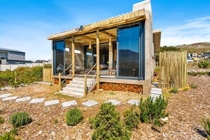 A modern house with a glass facade, a wooden deck, and a stone pathway leading to the entrance. - KOH Pringle Pod (Pringle Bay)