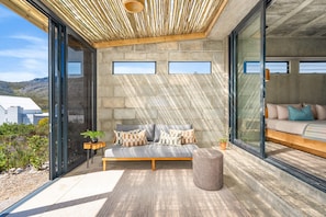 A modern outdoor seating area with a sofa and ottoman, a small table with a plant, and a view of the surrounding landscape. - KOH Pringle Pod (Pringle Bay)
