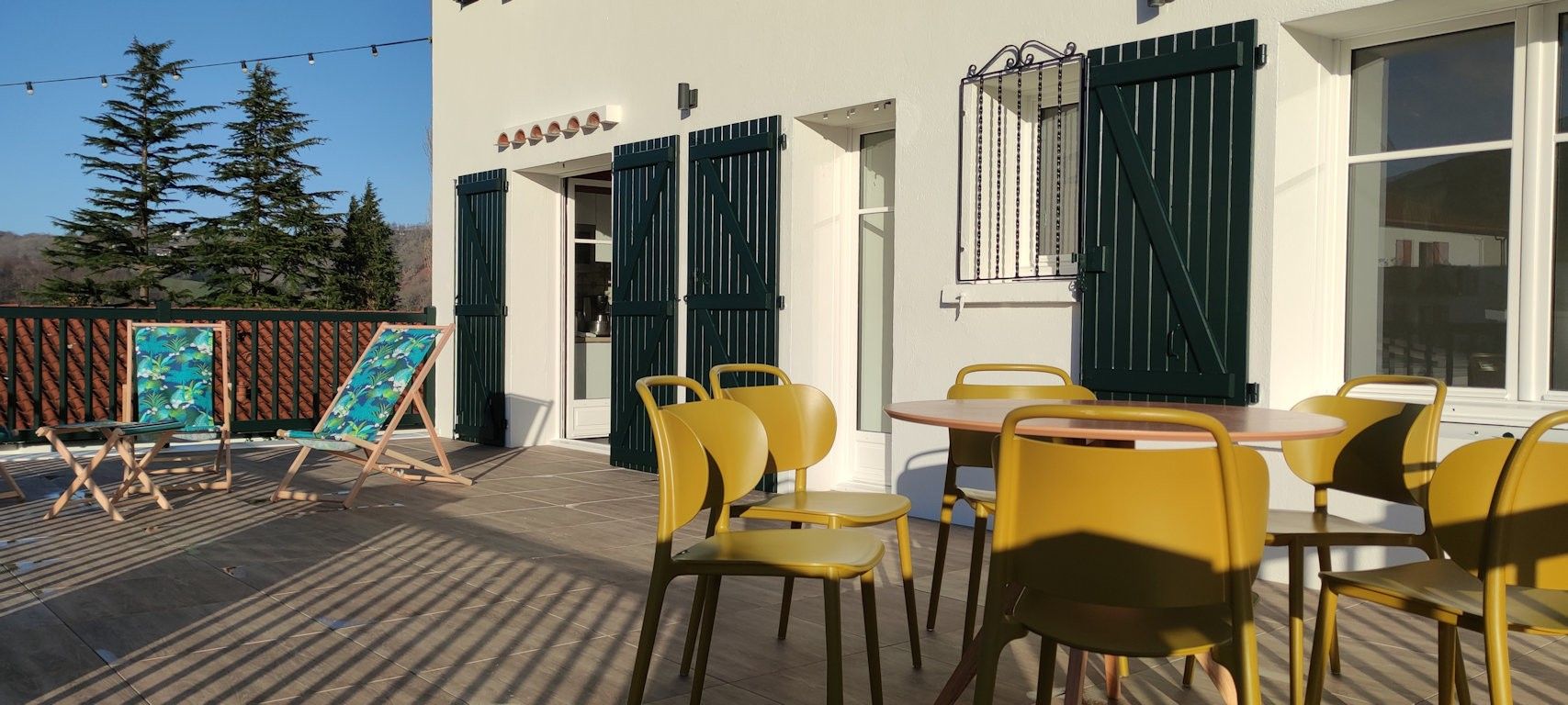 An outdoor seating area with yellow chairs and tables, a wooden deck, and a building with green shutters.