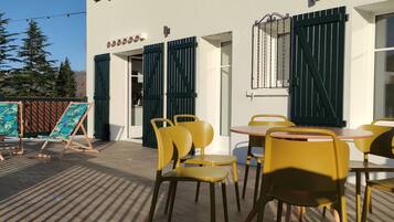 An outdoor seating area with yellow chairs and tables, a wooden deck, and a building with green shutters.