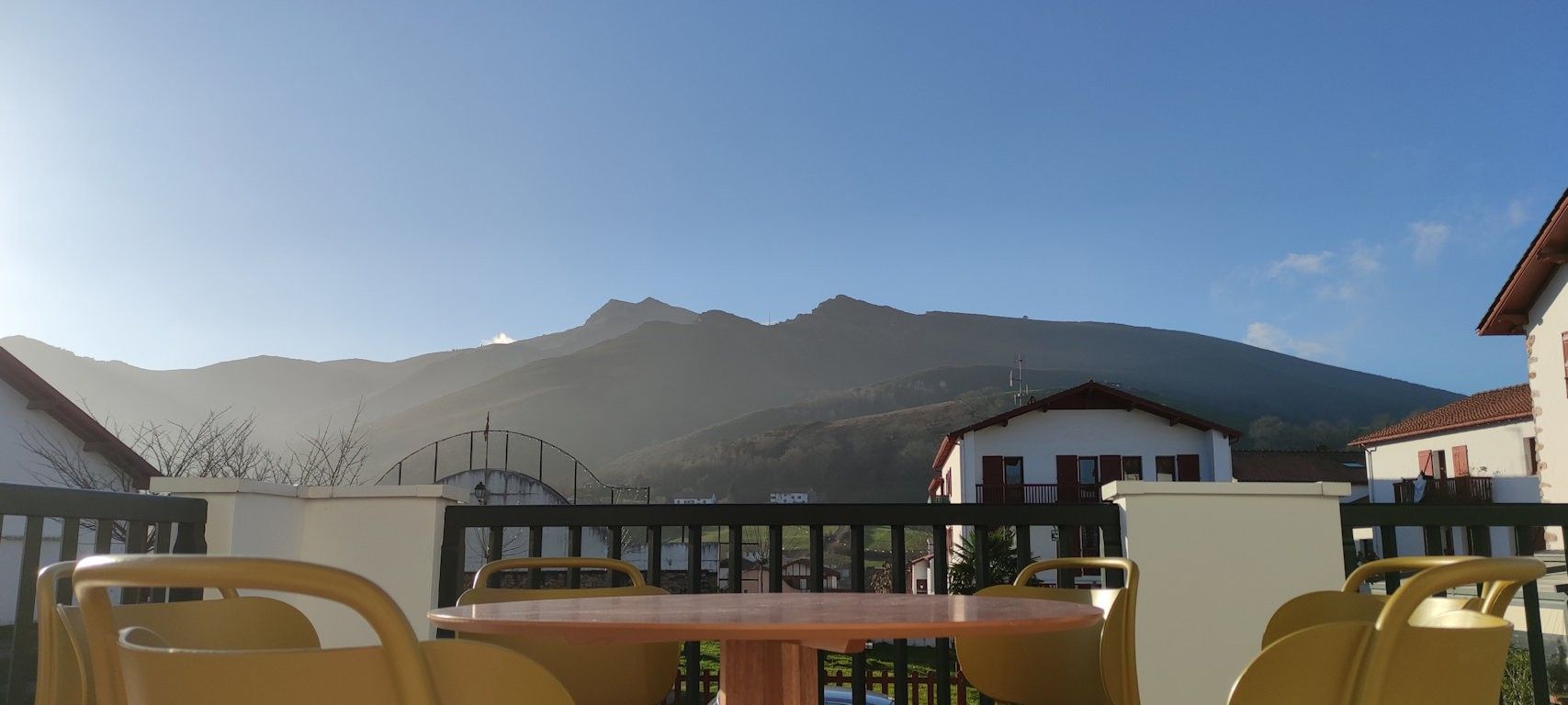 Eine Terrasse mit gelben Stühlen und einem Tisch, mit Blick auf ein Gebirge.