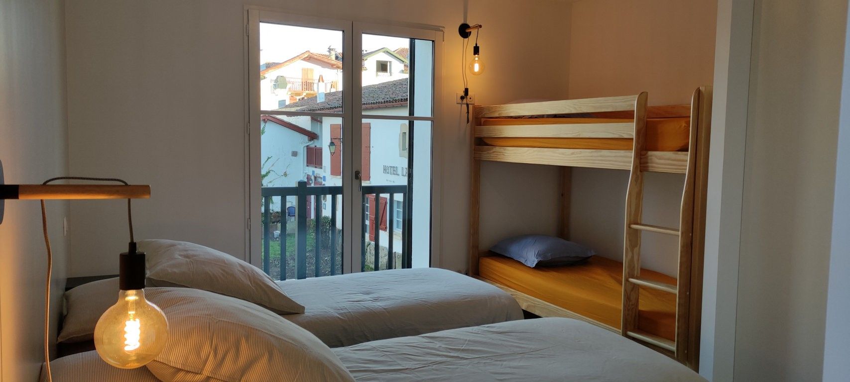 Ein Zimmer mit zwei Betten, einem Fenster mit Blick auf Gebäude und einer Pendelleuchte.
