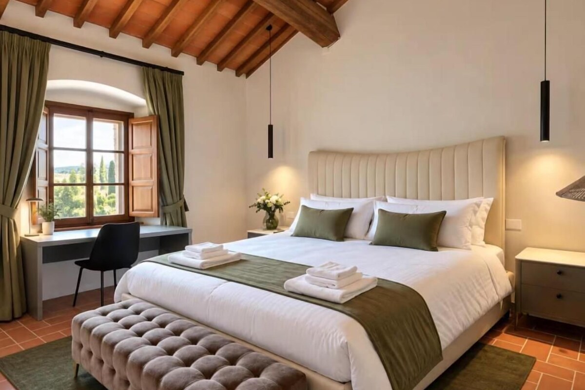 A bedroom with a large bed, a desk, and a window with curtains.