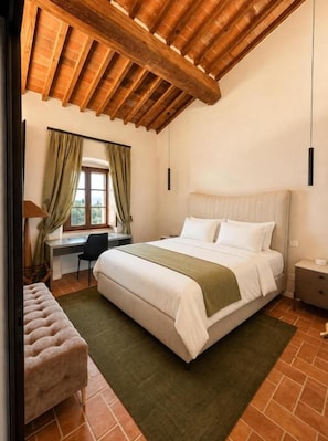 A bedroom with a large bed, a desk, and a chair. There is a window with curtains, a bench, and a hanging light fixture. - Villa Angelina (PROVINCIA DI AREZZO)