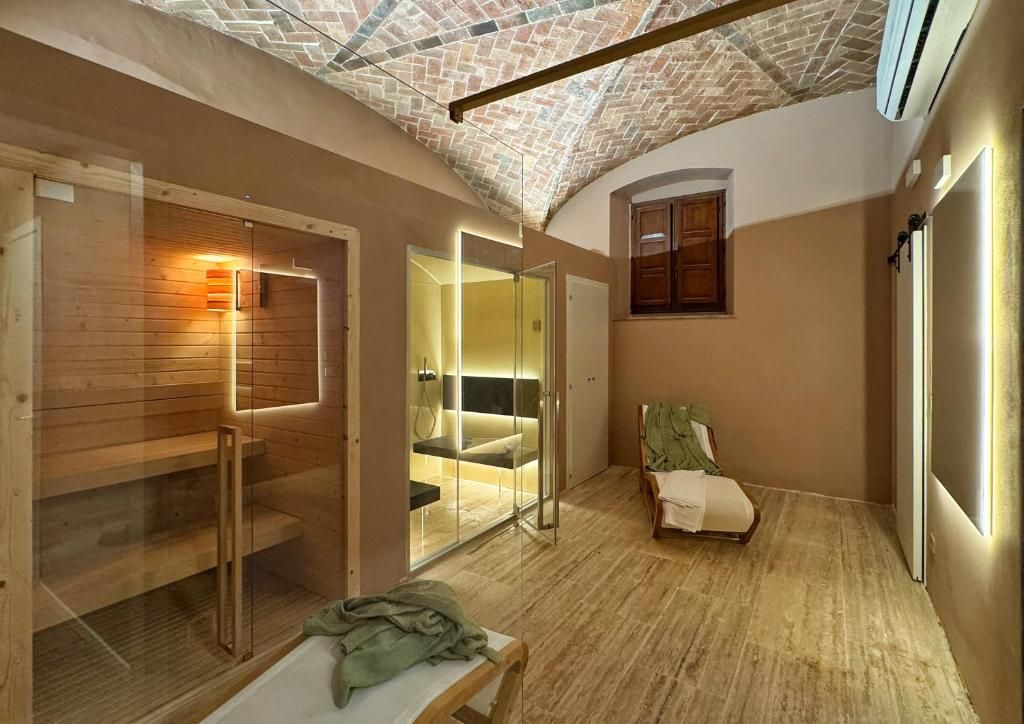 A room with a wooden floor, a glass door leading to a bathroom, a bed with a green blanket, and a wall-mounted air conditioning unit.