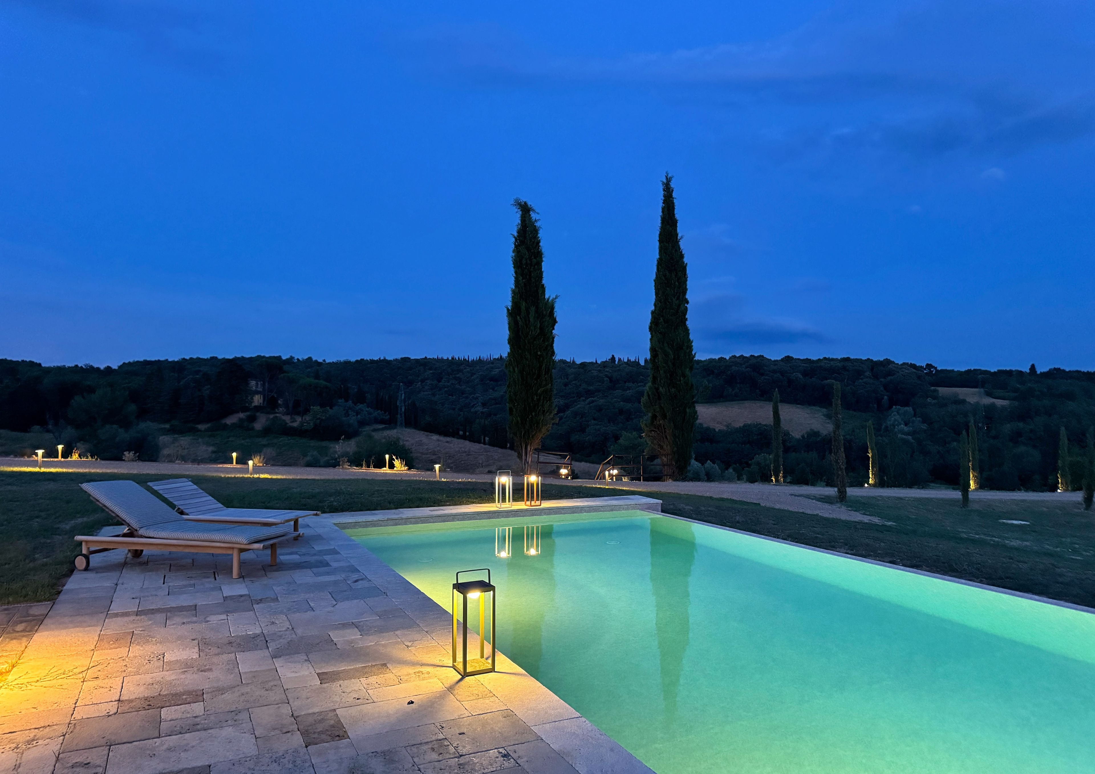A swimming pool with a lounge area and tall trees in the background.
