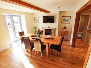 A dining area with a wooden table, chairs, a television, and a fireplace. - Three Chimneys (Lincoln)