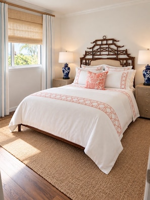 A hotel room with a large bed, wooden headboard, two bedside tables with lamps, a window with curtains, and a view of palm trees. - SHELL HOUSE - Old Florida Charm - Minutes to Historic Downtown Stuart & Beaches (Stuart)