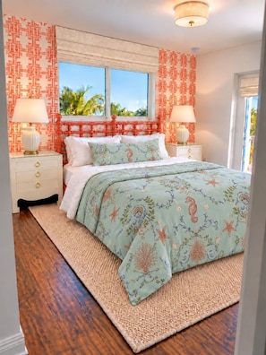 A bedroom with a bed, two bedside tables, a window with a view, and patterned wallpaper. - SHELL HOUSE - Old Florida Charm - Minutes to Historic Downtown Stuart & Beaches (Stuart)