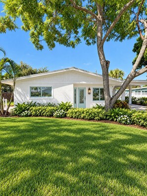 A single-story house with a white exterior, a front porch, and a well-maintained lawn. - SHELL HOUSE - Old Florida Charm - Minutes to Historic Downtown Stuart & Beaches (Stuart)