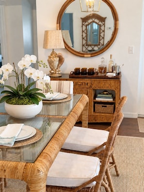 A dining area with a glass-top table, wicker chairs, a potted orchid, and a mirror on the wall. - SHELL HOUSE - Old Florida Charm - Minutes to Historic Downtown Stuart & Beaches (Stuart)