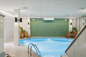 Una piscina interior con pared de azulejos, sillones de descanso y una escalera.