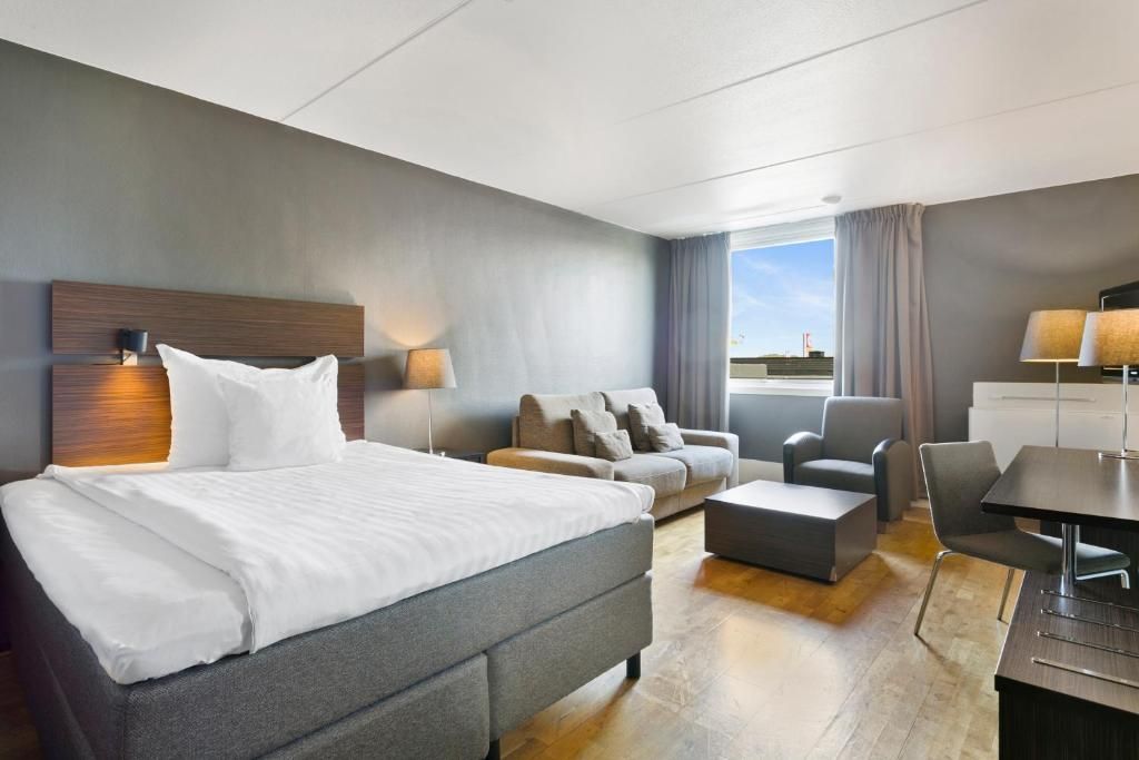 Ett modernt hotellrum med en stor säng, en soffa, ett skrivbord och utsikt över himlen.