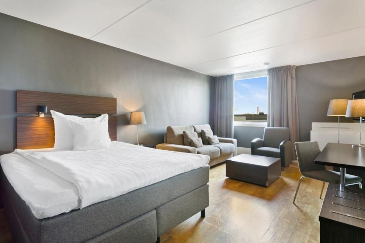 Habitación de hotel moderna con una cama grande, un sofá, un escritorio y vistas al cielo.