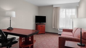 Ein Hotelzimmer mit Schreibtisch, Stuhl, Fernseher, Sofa und einem kleinen Tisch.