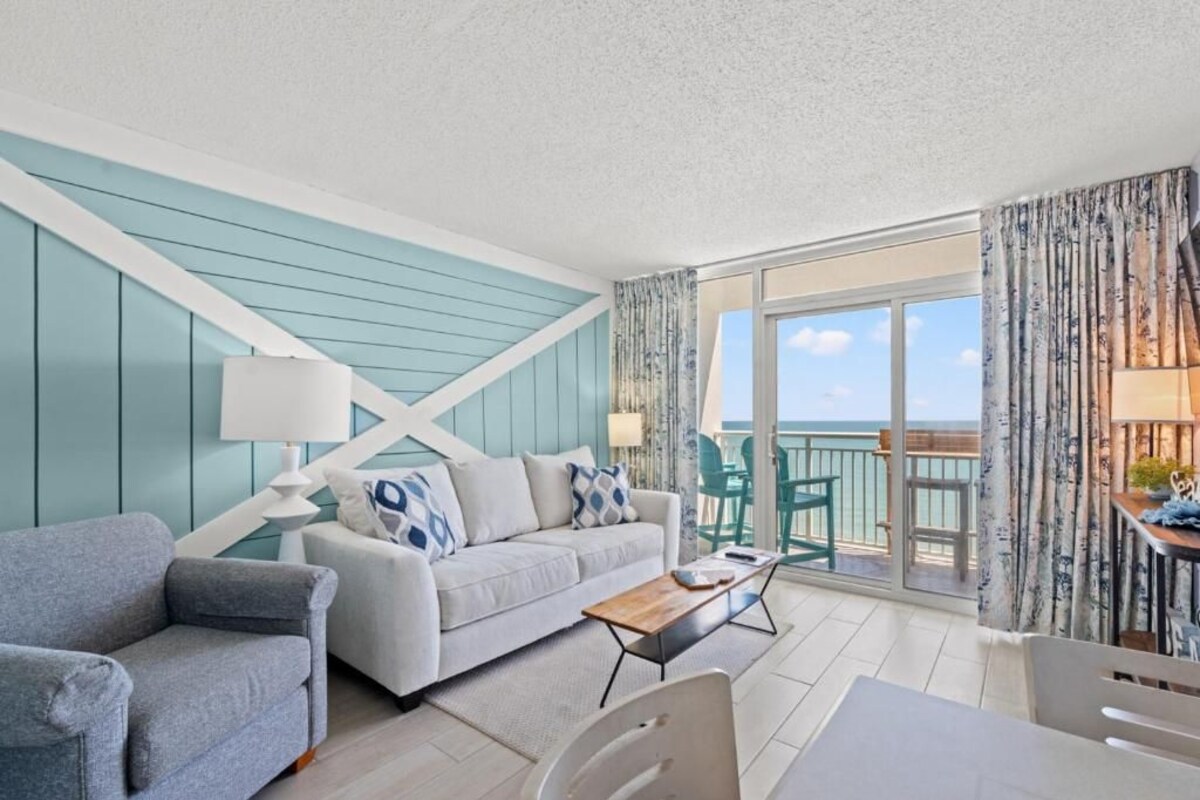 A modern living room with a sofa, coffee table, and a view of the ocean through a sliding glass door.