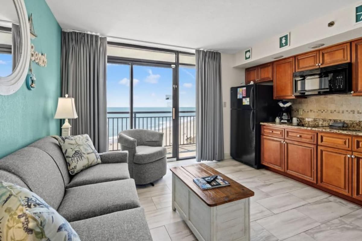 Ein modernes Hotelzimmer mit Balkon, einer Couch, einem Couchtisch und einer Küchenzeile.
