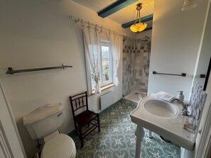 Un bany amb vàter, una cadira de fusta, plat de dutxa amb porta de vidre i un lavabo amb mirall.