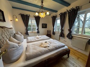 A bedroom with a large bed, two bedside tables, a chandelier, and curtains on the windows. - Det Danske Hus - Apartment Starboard (Dunsum)