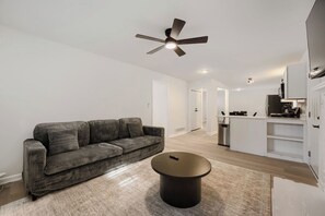 A modern living room with a sofa, a coffee table, and a ceiling fan. - Cozy Atlanta Getaway | 3 Bedroom Near Airport (East Point)