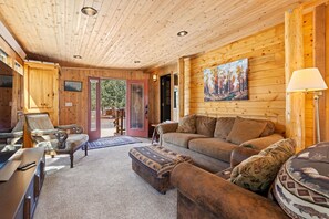 L’intérieur chaleureux d’un chalet avec des murs en bois, un canapé, un fauteuil et un tableau accroché au mur.
