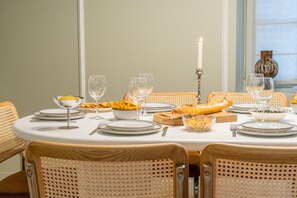 Una mesa de comedor dispuesta con platos, tazones, cubiertos y vasos, rodeada de sillas de mimbre.