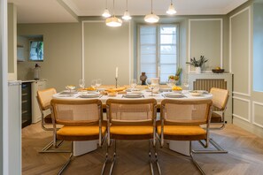 Un coin repas avec une table ronde dressée pour six personnes, entourée de chaises en osier dotées d’assises rembourrées.