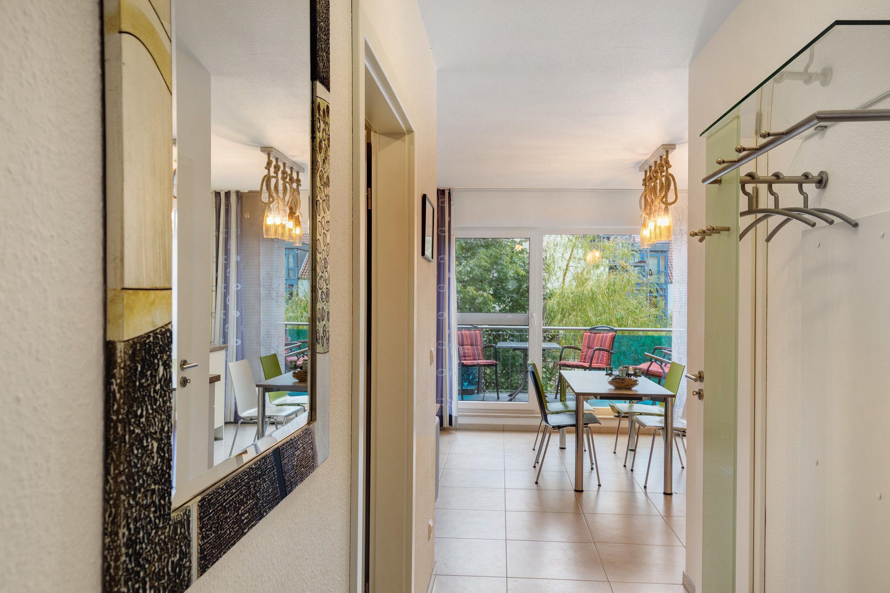 Un pasillo que conduce a un balcón con comedor, puerta de cristal y lámpara colgante.