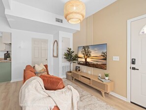 A modern living room with a large flat-screen TV, a sofa, a coffee table, and a decorative wall piece. - Lake Toho Haven | Vintage Boho Style & Park Views (Kissimmee)