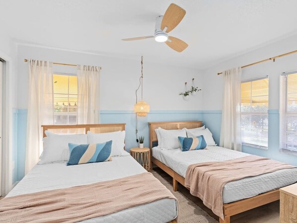 Une chambre avec deux lits, un ventilateur de plafond et une table de chevet avec une lampe.