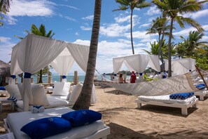 Eine Strandlounge mit weißen Markisen, weißen Liegestühlen und blauen Kissen.
