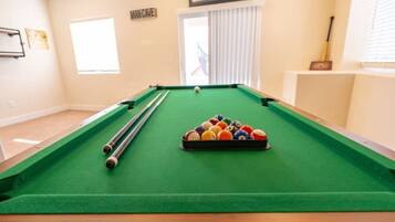 A pool table with balls and cues, a window with blinds, and a door labeled 'MANCAVE.'