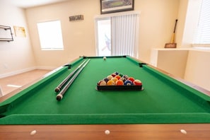 A pool table with balls and cues, a window with blinds, and a door labeled 'MANCAVE.'