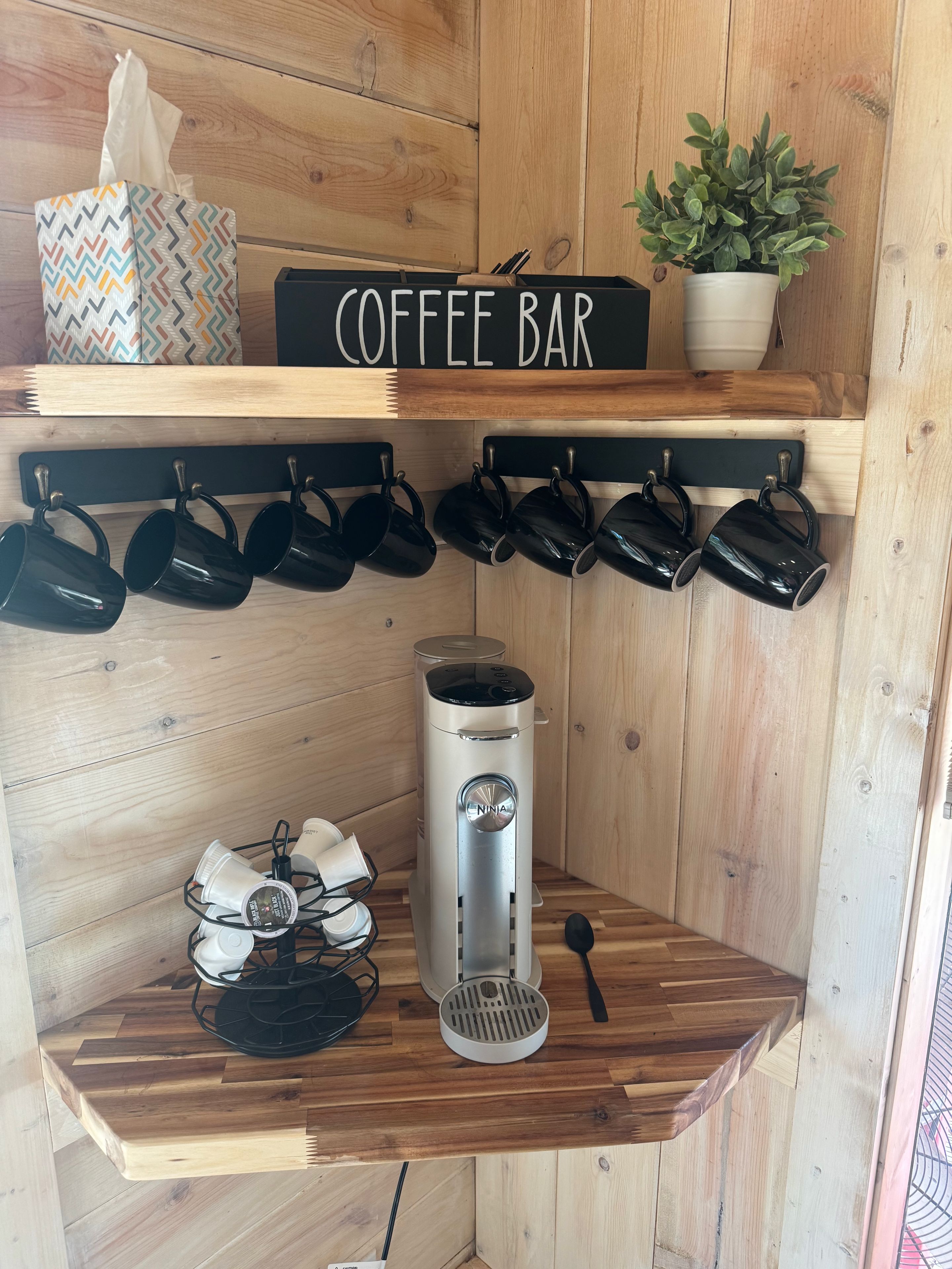 Un espace bar à café avec un panneau, des tasses, une machine à café et une plante.