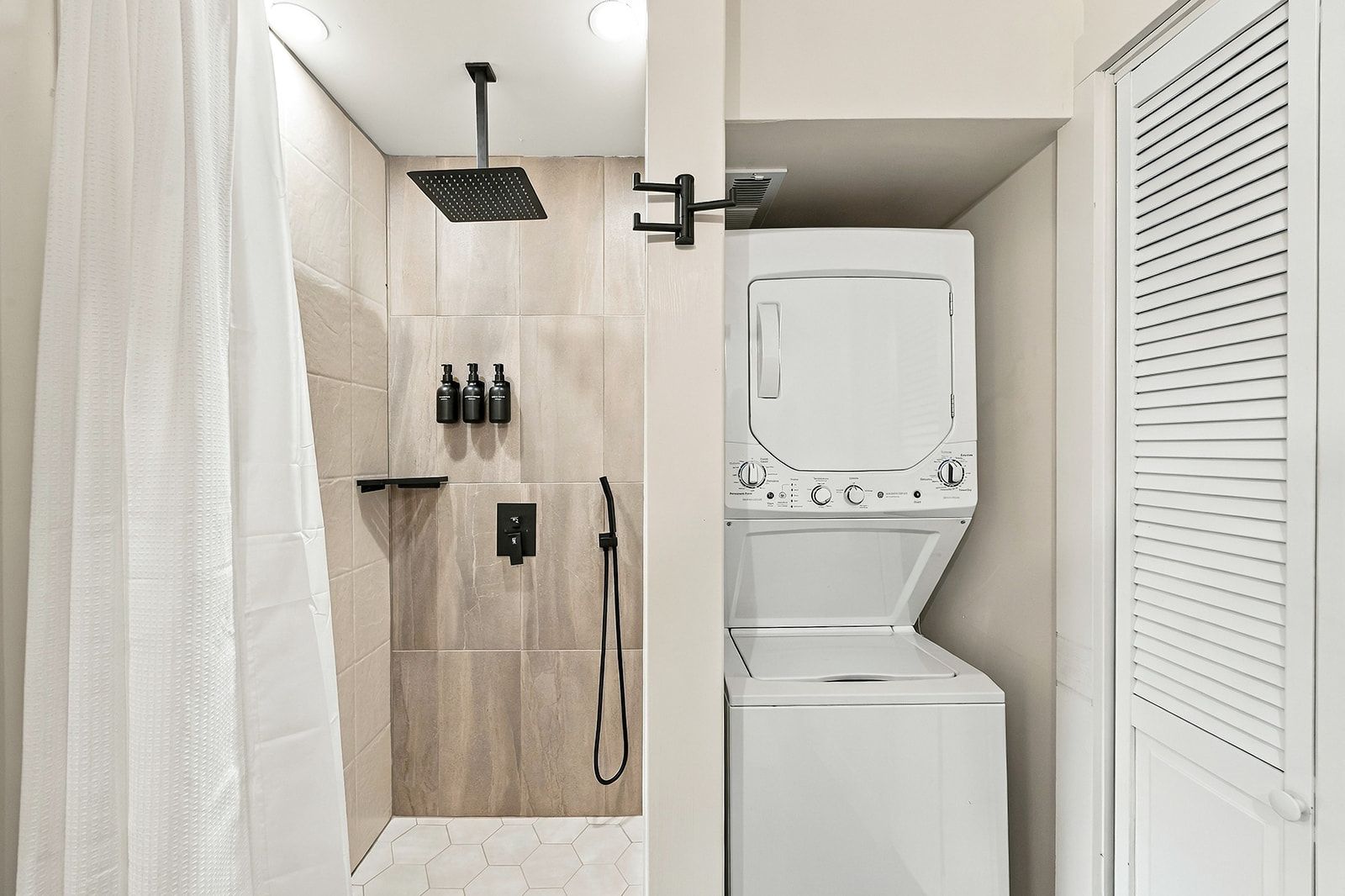 A compact bathroom with a shower, a built-in washer, and a towel rack.