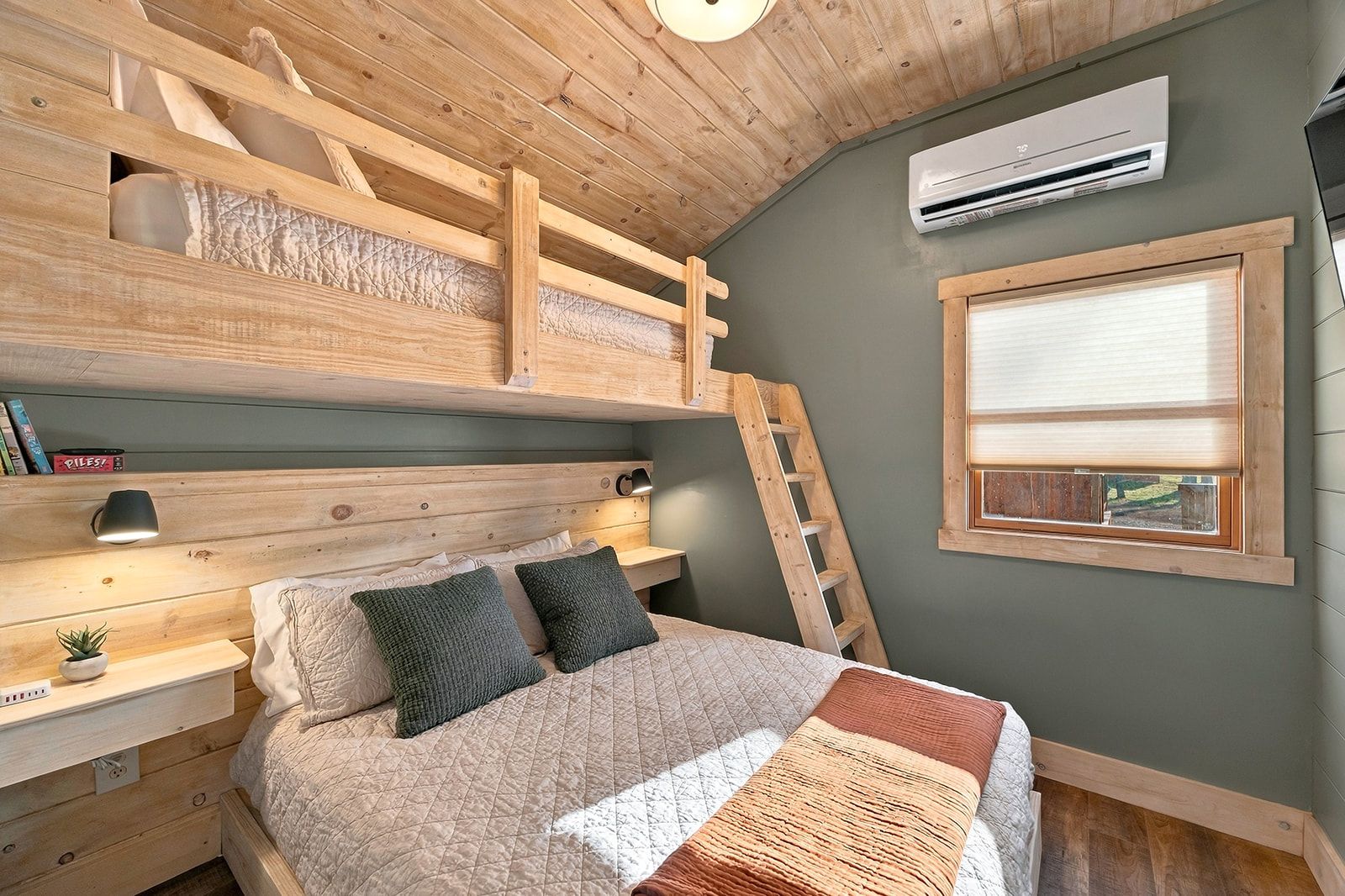 Une chambre avec un lit superposé, une table de chevet avec une lampe, une fenêtre avec des stores et un appareil de climatisation.
