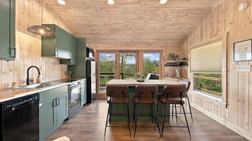 A kitchen with a central island, bar stools, and a view of the outdoors.