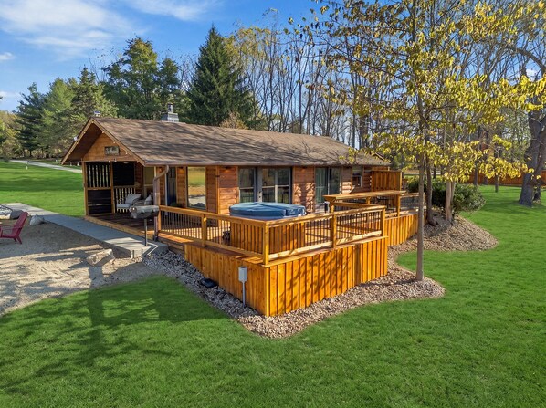 Una cabaña de troncos con un porche, mobiliario exterior y un jacuzzi.