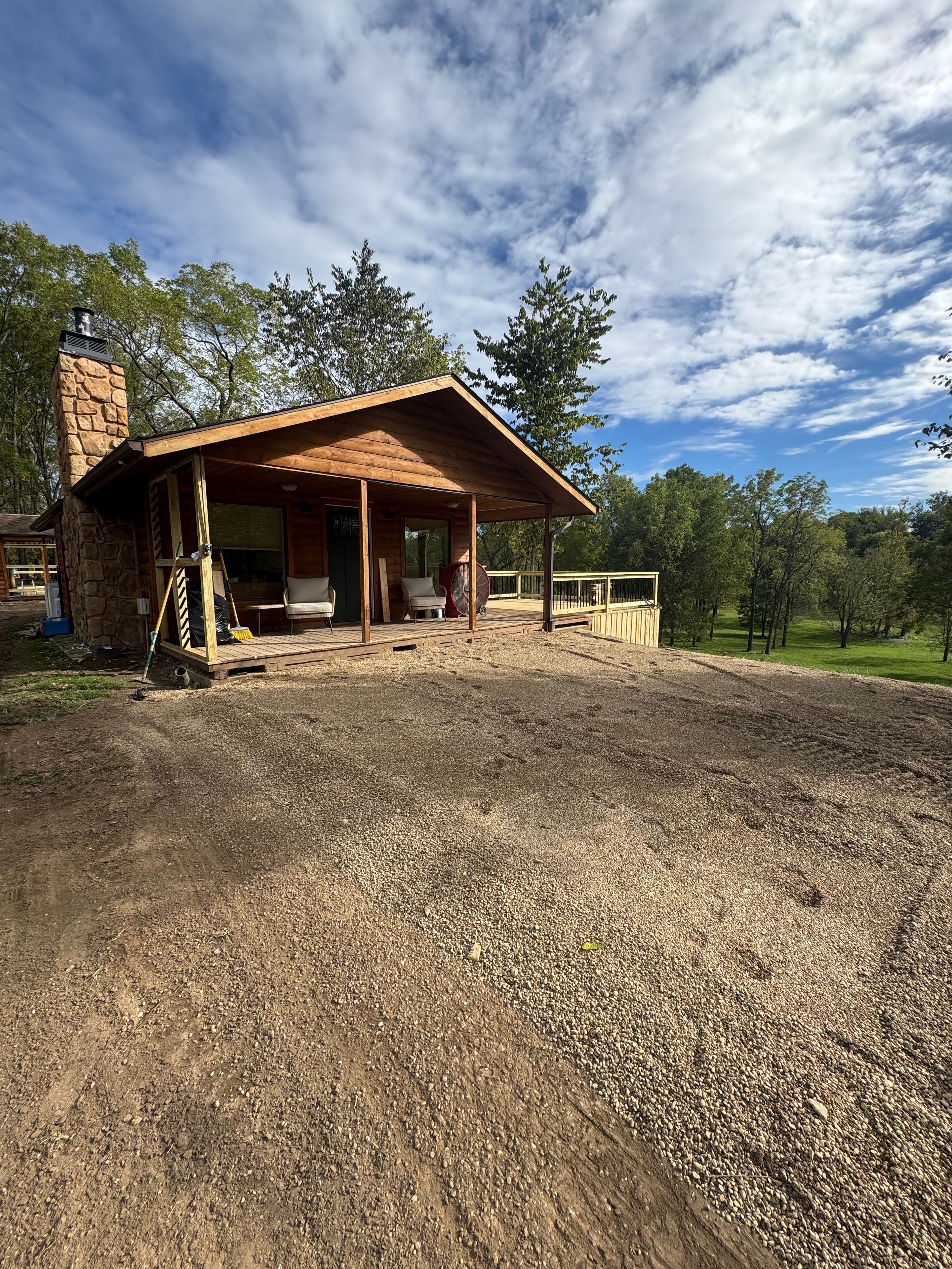 A rustic cabin with a covered porch, stone chimney, and a gravel driveway.