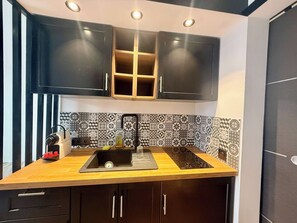 A kitchen with a wooden countertop, black cabinets, a black sink, and patterned backsplash tiles. - B087 Appartement cosy et moderne – Terrasse-Centre-ville (Cannes)