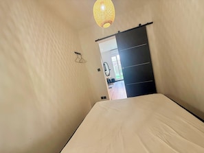 A bedroom with a bed, a door leading to a bathroom, and a hanging light fixture. - B087 Appartement cosy et moderne – Terrasse-Centre-ville (Cannes)